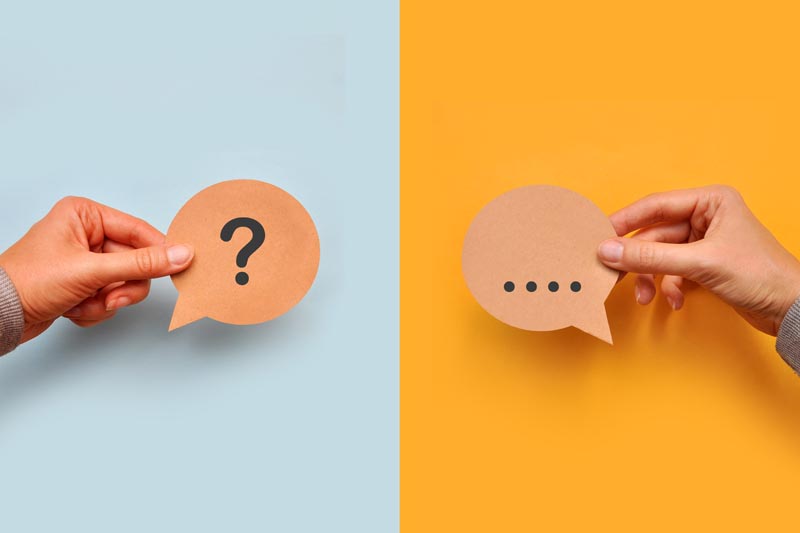 Zwei Hände halten je eine Sprechblase aus braunem Papier, links mit Fragezeichen vor hellblauem Hintergrund, rechts mit Auslassungspunkten vor orangefarbenem Hintergrund