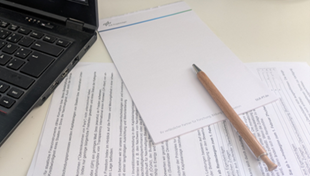 ein aufgeklapptes Notebook, ein Stift und ein Noitzblock im DLR-PT Design